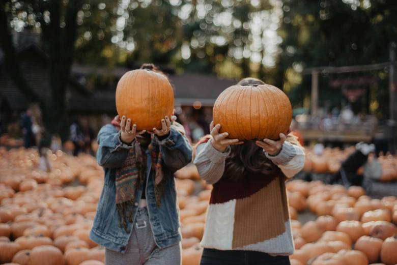 Two people holding pumpkins in front of their heads at a pumpkin patch - Fall bucket list ideas. 