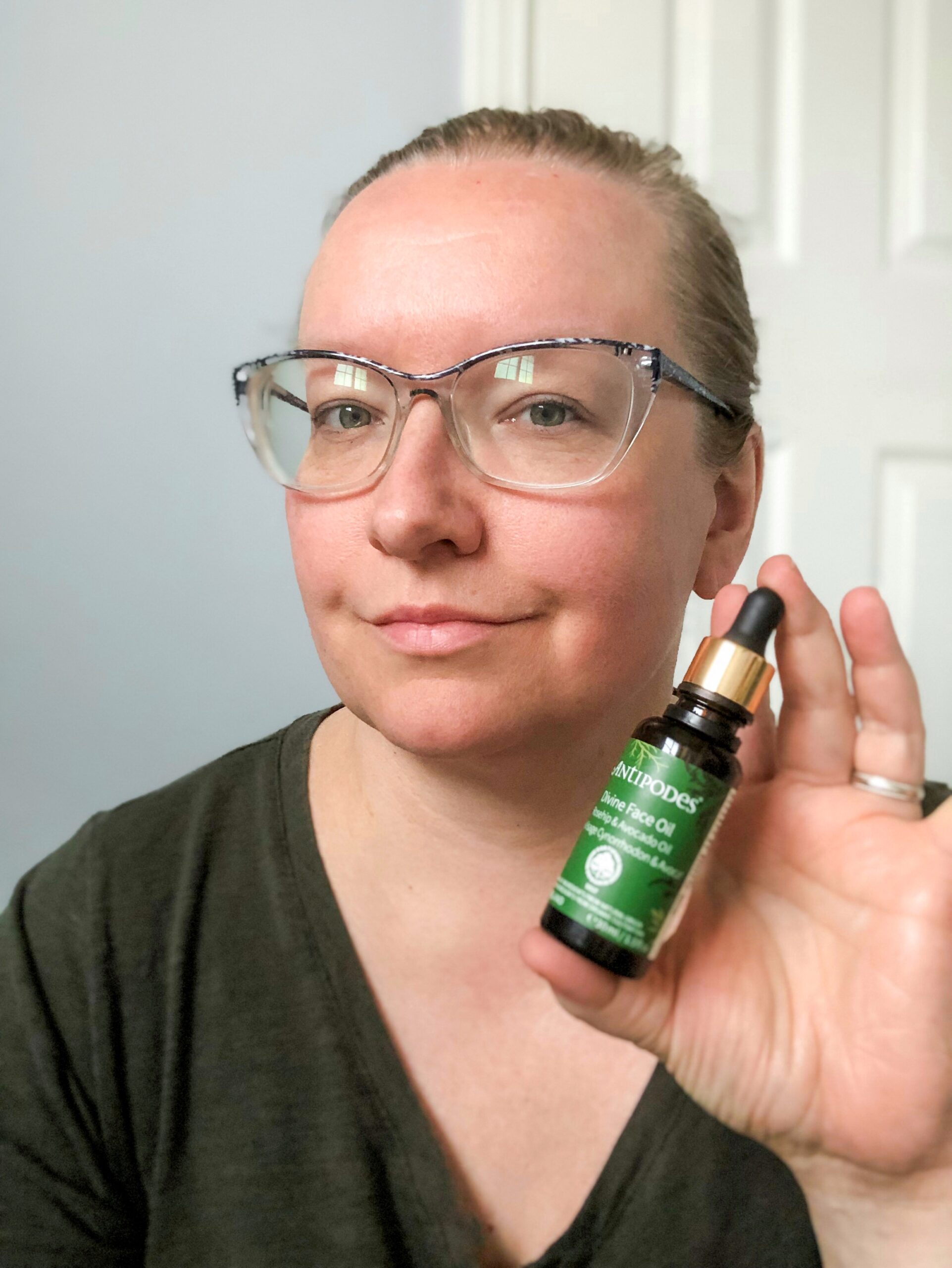 Woman holding a bottle of Antipodes face oil - gua sha face massage routine. 