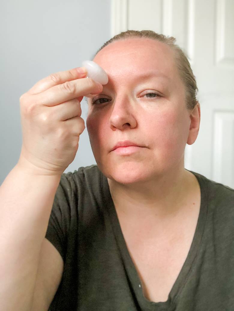 Woman using an eye depuffer - gua sha face routine. 