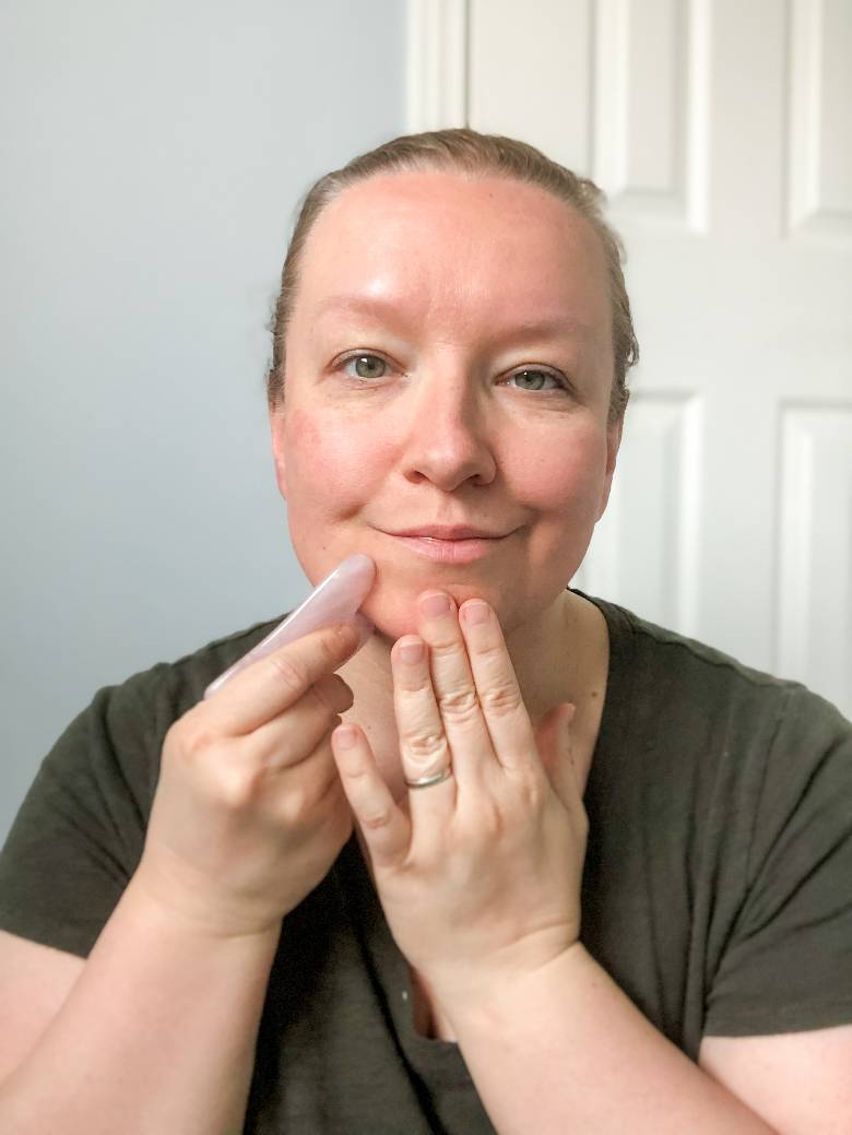 Woman using a gua sha tool on her face - gua sha routine. 