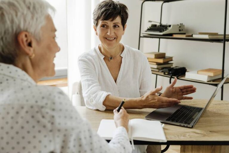 Two women talking at a desk with a notepad - how to become your own boss after retirement.