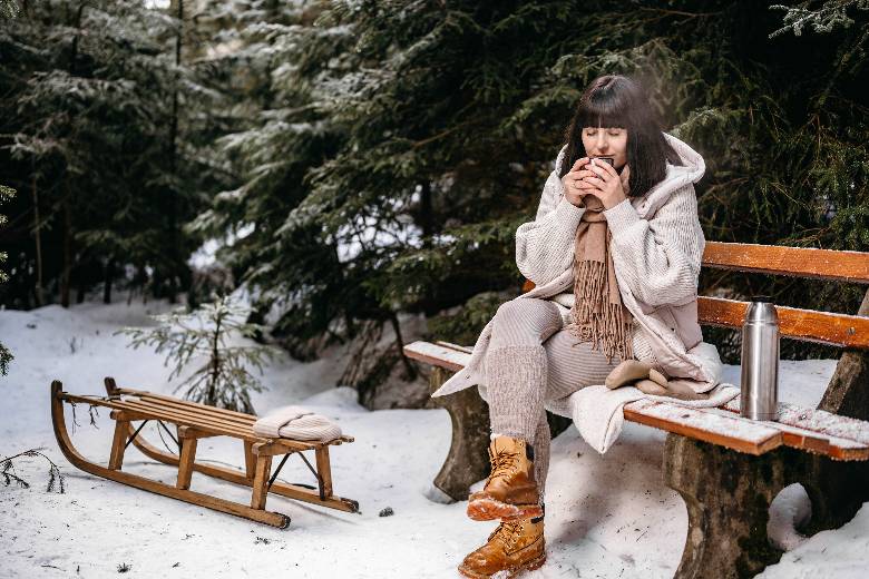 Woman in a winter coat, sipping something out of a cup in a winter setting. 