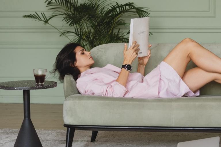 A woman relaxing on a sofa, reading a book - how to get back to a productive routine when you've been distracted.