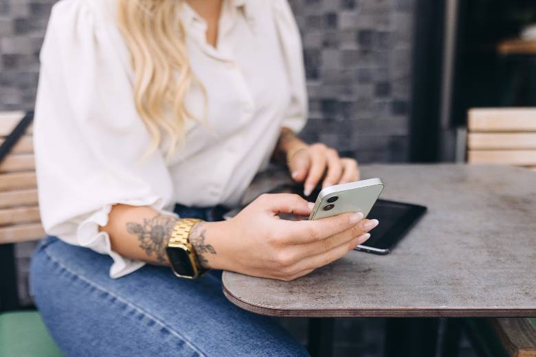 Woman sitting at a table, using a phone - reasons for starting at business at 40.