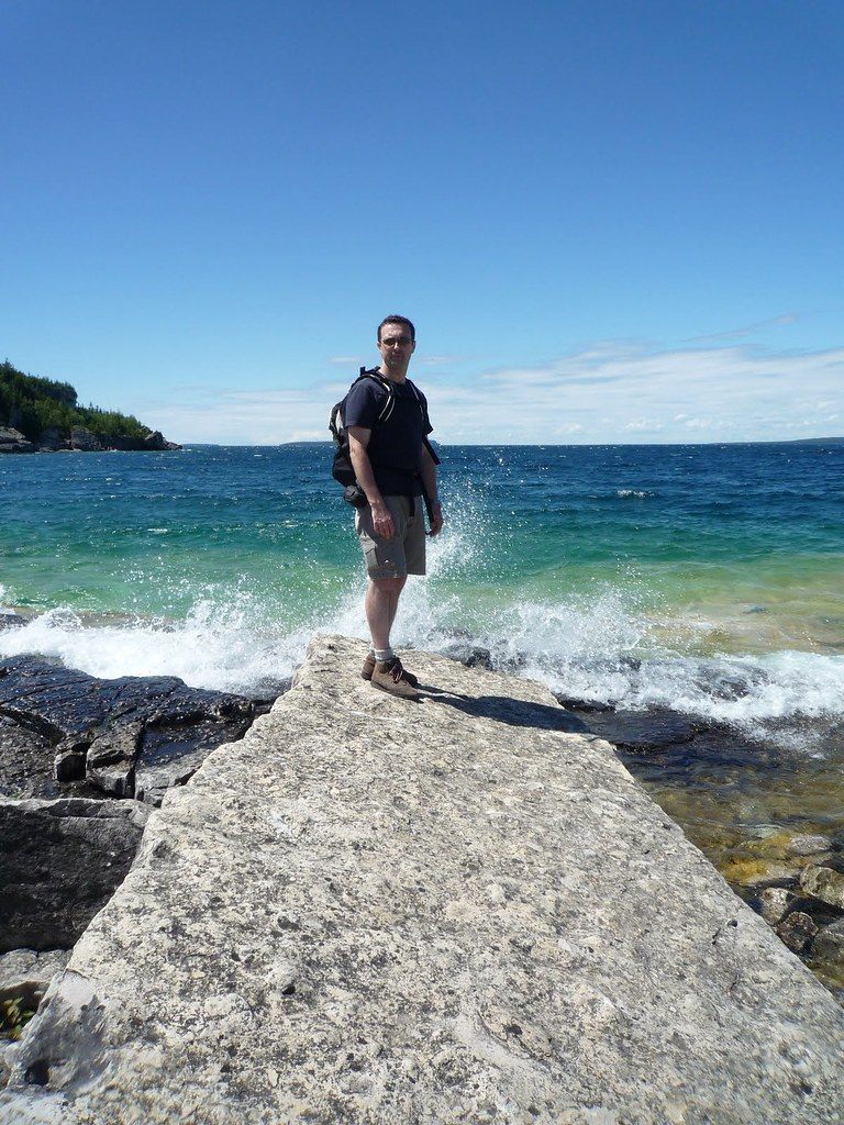 Standing near The Grotto, at Bruce Peninsula National Park, close to the Marr Lake Trail. Man about to get splashed by the wave at the shoreline. 