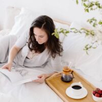 Woman laying on a bed with a coffee on a tray - ways to be happier in your 40s.