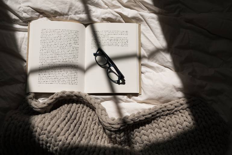 Open book and glasses on a bed - winter self-care ideas.